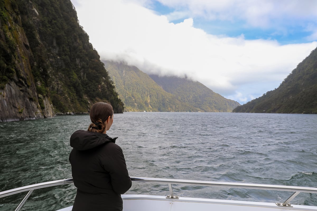 Woman looking across Milford Sound from the bow of a cruise boat surrounded by steep mountains