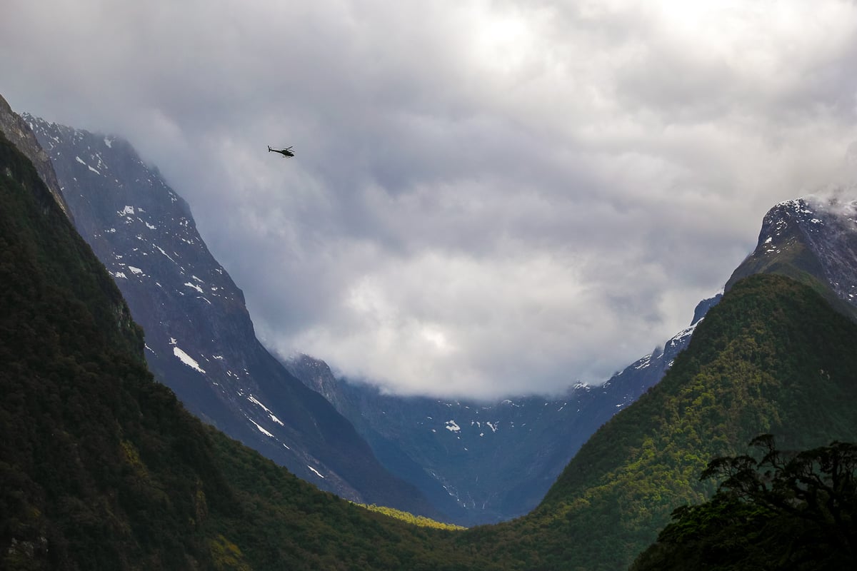Helicopter flying above the dramatic snow-dusted mountains and rainforest in Fiordland National Park