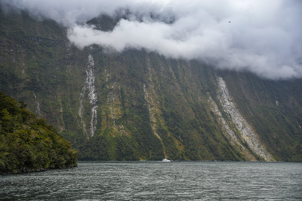 Low clouds hanging over steep rainforest-covered cliffs and waterfalls in New Zealand