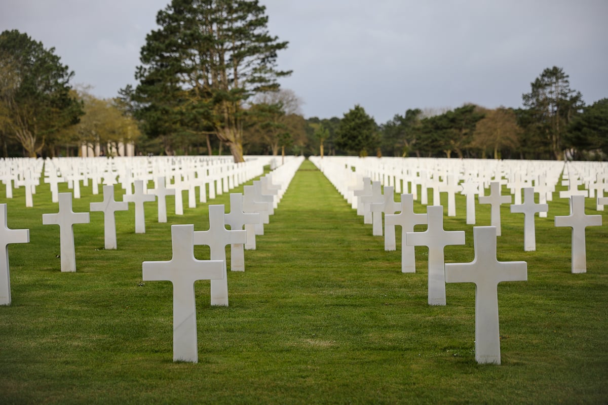 Rows of white marble crosses stretching across the manicured green lawn at Normandy American Cemetery in Colleville-sur-Mer, France, commemorating American soldiers who died during World War II.
