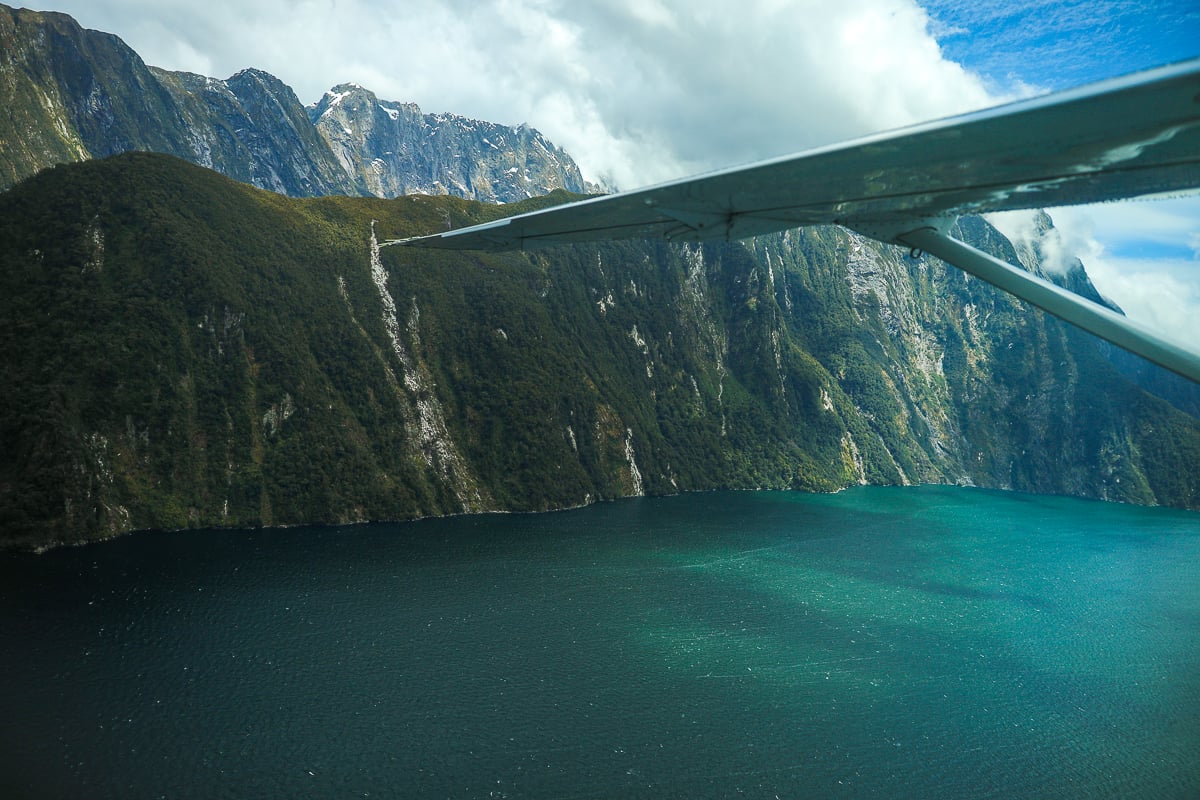 Scenic flight over Milford Sound with turquoise water, towering cliffs and waterfalls below