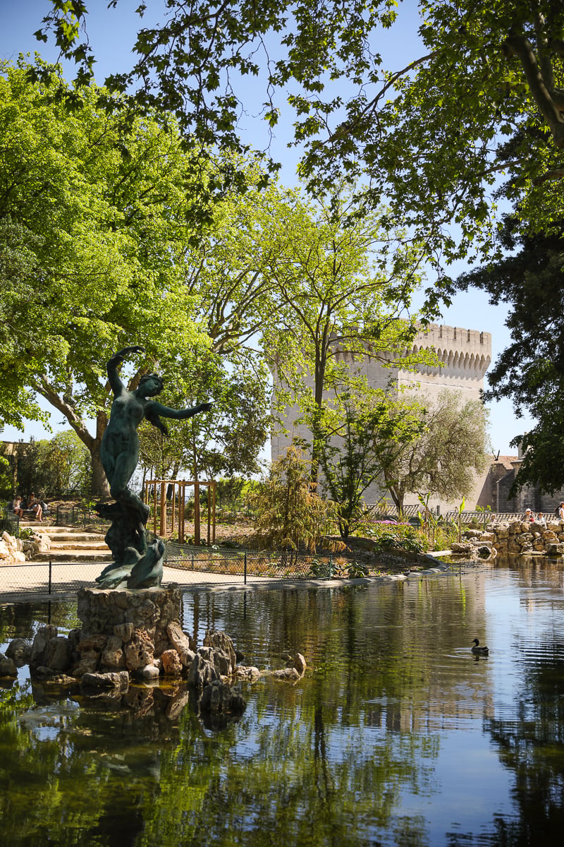 Pond and bronze statue in Jardin des Doms with the Palais des Papes behind the trees