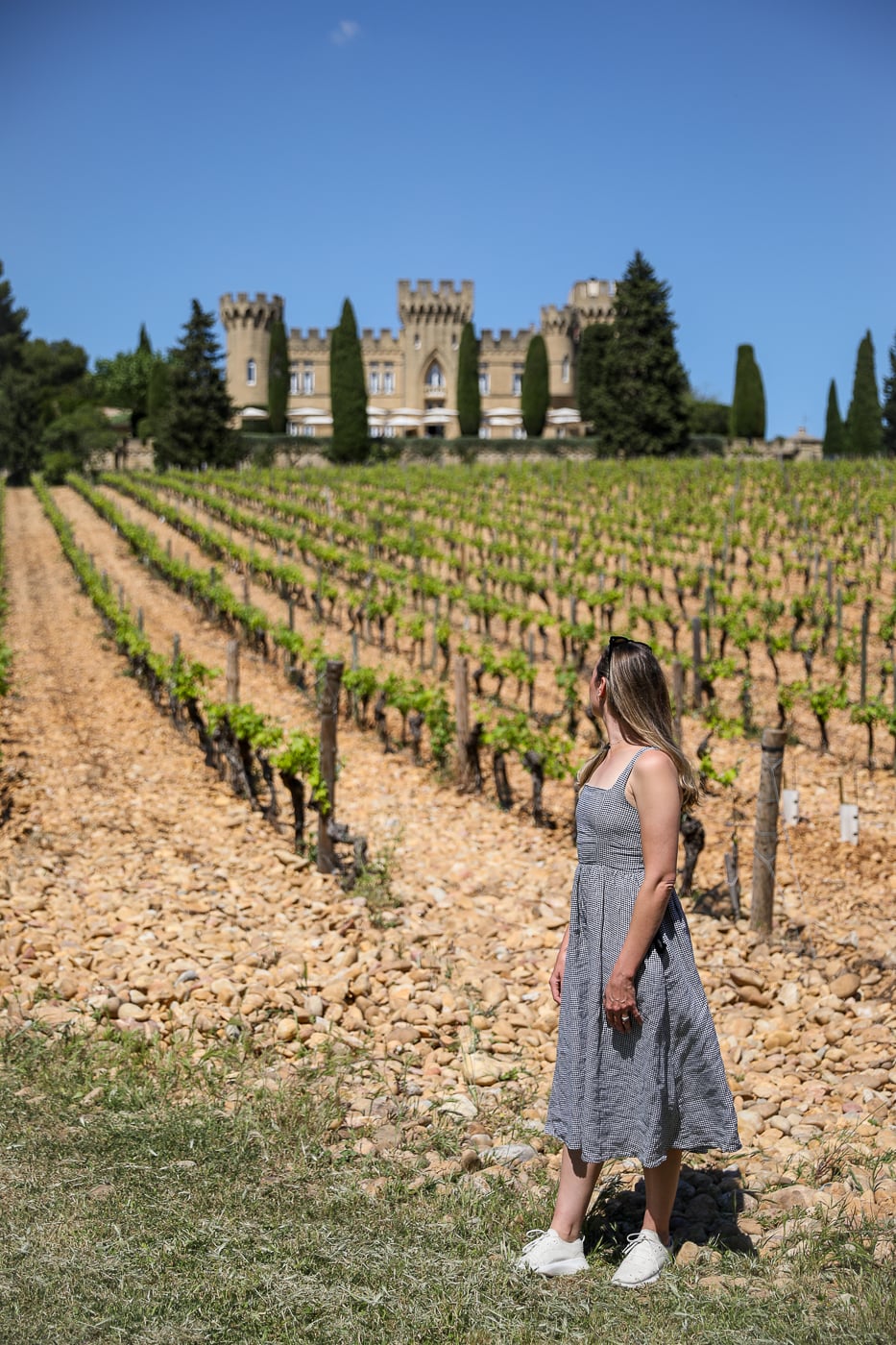 Traveler standing among Châteauneuf-du-Pape vineyards with Château des Fines Roches behind